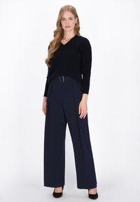 Pullover navy a V abbinato a pantaloni navy a gamba larga con vita alta. Tessuto testurizzato, dettaglio della cintura minimalista e tacchi neri completano il look.
