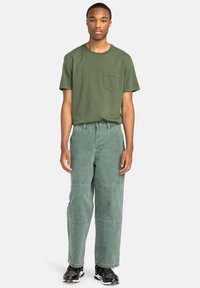 Green cotton t-shirt with a chest pocket, paired with loose-fitting green pants featuring a textured finish and visible stitching details.