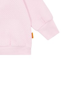Sudadera de color rosa claro con un patrón texturizado, puños acanalados y una pequeña etiqueta de logo en el costado. Tejido suave con una apariencia acogedora.