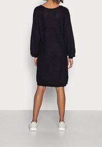 Abito nero lavorato a maglia con vestibilità ampia, spalle scese e maniche lunghe. Caratterizzato da una texture a costine e una silhouette leggermente oversize.