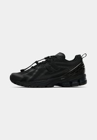 Chaussure de sport noire avec un système de verrouillage des lacets, semelle rembourrée et panneau latéral avec logo, présentée sur un fond clair et uni.