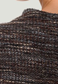 Pull en tricot présentant un mélange de fils noirs, bruns et gris avec un motif texturé et des accents métalliques, col rond et tissage ouvert.