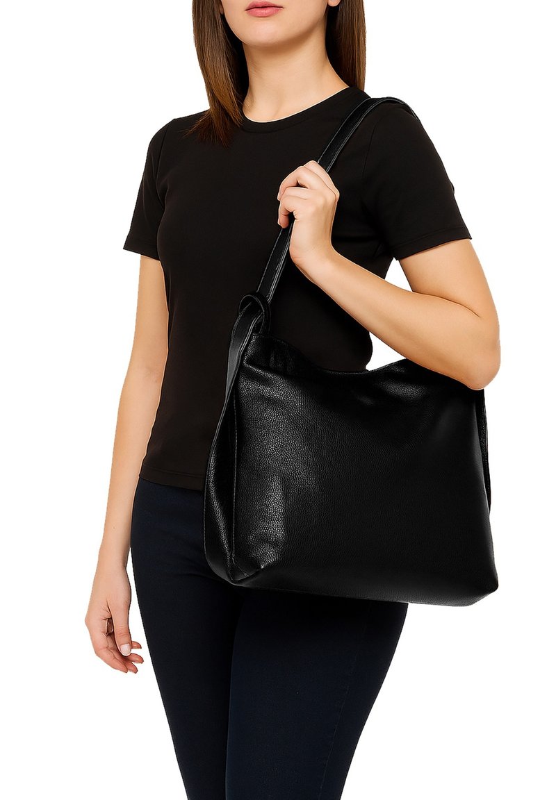 Schwarze Lederschultertasche mit glatter Oberfläche, großem Fassungsvermögen und einem einzigen Riemen, gehalten von einer Person, die ein schwarzes T-Shirt und dunkle Jeans trägt.