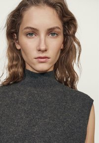 Dunkelgrauer ärmelloser Rollkragenpullover aus weichem, strukturiertem Strick, mit hohem Kragen und klaren Linien. Keine sichtbaren Muster oder Akzente.