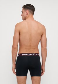 Čierne atletické nohavice s bordovou a bielou elastickou páskou s logom Nike. Hladká textúra, priliehavý strih a dĺžka po stred stehna.