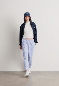 Igapäevane outfit, kus on tumesinine müts, valge lukuga sviiter ja helesinised dressipüksid pahkluu mansettidega. Moodne inimene kannab valgeid hiina tossusid.