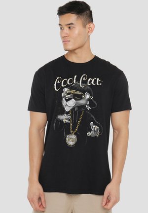 Junger Mann trägt ein schwarzes T-Shirt mit einem Grafik eines Katers in Sonnenbrille, Hut und Goldkette mit dem Text "Cool Cat" auf einem grauen Hintergrund.