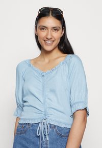 Blusa de algodão de manga curta, azul claro, com decote franzido, cintura ajustada e cordão ajustável na barra.