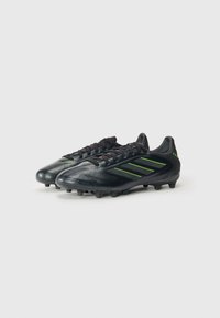 Black soccer cleats with green accents, featuring a textured upper, lace-up front, and molded studs for traction on grass surfaces.