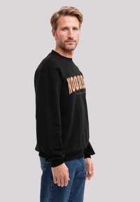 Schwarzer Sweatshirt mit einem ausgebleichten orangefarbenen "NOORD"-Grafik auf der Vorderseite, Rundhalsausschnitt, gerippten Bündchen und einem lockeren Schnitt.