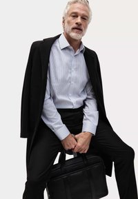 Zwarte overjas, lichtblauw gestreept shirt, zwarte broek. Man houdt een zwarte leren tas met handvatten vast. Gladde textuur, op maat gemaakt.