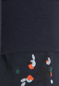 Tejido de punto azul marino oscuro con textura acanalada, que presenta patrones bordados coloridos de formas en naranja, verde, azul y blanco.