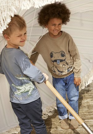 Two children under a white umbrella. One wears a taupe sweatshirt with a frog design; the other has a blue shirt with an alligator print.