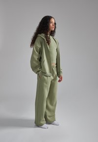 Set di abbigliamento attivo di verde chiaro composto da una felpa ampia, un top aderente e pantaloni a gamba larga realizzati in un morbido tessuto testurizzato.