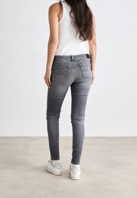 Vaqueros ajustados en denim gris, con cintura de talle medio, diseño de cinco bolsillos y detalles de costura sutiles, combinados con zapatillas blancas.