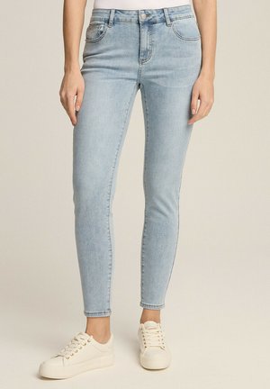 Jasnoniebieskie dżinsy skinny z średnim stanem, posiadające przednie i tylne kieszenie, szlufki na pasek oraz gładką teksturę denimu. W zestawieniu z białymi trampkami.