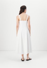 Robe midi blanche avec bretelles réglables, corsage ajusté, dos ouvert et jupe évasée. Tissu lisse et léger avec un design épuré et minimaliste.