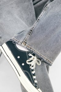 Sorte lærreds sneakers med hvide snørebånd, der har et klassisk lavt design. Båret sammen med lys grå jeans, der er slidt ved kanten og viser en afslappet stil.