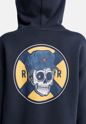 Felpa con cappuccio blu navy con un grande motivo grafico di un teschio con un berretto blu, un occhio rosso e uno sfondo giallo, incorniciato da un design circolare.