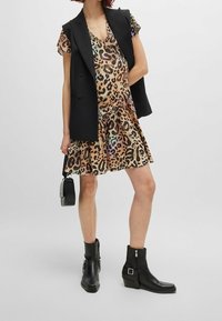 Robe imprimée animal avec des manches courtes, dans des nuances de marron et de noir, avec un ourlet volanté. Assortie à un blazer sans manches noir et des bottines.