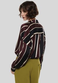 Blusa a maniche lunghe con motivo a righe in bordeaux, nero e crema. Realizzata in satin con una vestibilità rilassata e dettaglio di tasca sul retro.