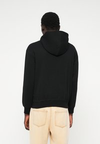 Μαύρη φούτερ με κουκούλα και άνετη εφαρμογή, με ραμμένα μανίκια, συνδυασμένη με ανοιχτόχρωμα τζιν που διαθέτουν πίσω τσέπες.