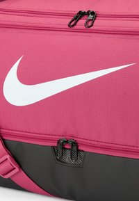 Nike sporttas in roze stof met een wit logo, zwarte basis, twee ritsen en een gevoerde schouderband voor comfortabel dragen.