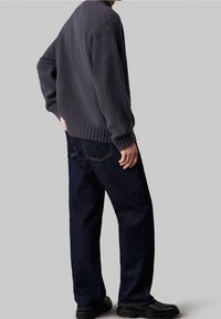 Szary teksturowany sweter z prążkowanymi mankietami, zestawiony z ciemnoniebieskimi dżinsami. Czarny obuwie dopełnia strój.