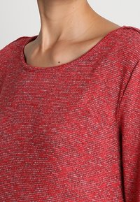Czerwony sweter z dzianiny z szerokim dekoltem i teksturowanym materiałem, z kombinacją czerwonych i szarych nici w luźnym kroju.