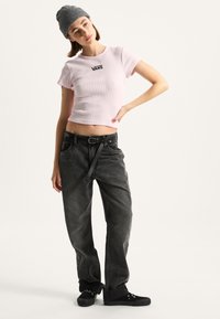 Rosa gerippter Crop-Top mit schwarz "VANS"-Logo, kombiniert mit schwarzen hochtaillierten Jeans und schwarzen Sneakers. Das Modell trägt eine gestrickte graue Mütze.