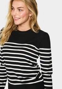 Maglione a righe bianco e nero con colletto tondo, caratterizzato da maniche lunghe e tessuto a maglia testurizzato. Le righe variano in larghezza.
