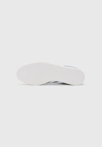 Semelle extérieure de sneaker blanche avec une surface texturée hexagonale, présentant des accents bleus et trois bandes sur le côté, fabriquée en matériau en caoutchouc.