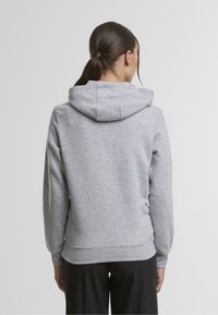 Sivá mikina s kapucňou a uvoľneným strihom, ktorá sa vyznačuje jemnou textúrou, rebrovanými manžetami a kapucňou na stiahnutie. Zadná časť je bez švov a má zakrivený lem.