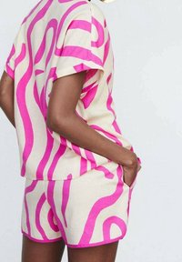 Ensemble deux-pièces en lin avec un fond beige orné de motifs ondulés fuchsia audacieux. Le haut a des manches courtes, et le short possède des poches latérales.