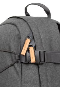 Sac à dos en tissu gris avec une forme arrondie, équipé de matériel noir et de tirettes de fermeture éclair en cuir. Comprend une poignée supérieure et des sangles latérales.