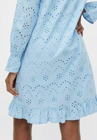 Šviesiai mėlyna suknelė su aklėmis, raukšlėtu apvadu ir ilgomis rankovėmis. Audinys atrodo tekstūruotas, rodo gėlių raštus ir atvirus dizainus.