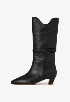 Botte en cuir noir mi-mollet avec un bout pointu, un talon bas incliné, une tige légèrement froncée et un bord supérieur courbé.