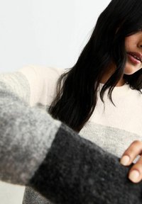 Pull en tricot avec des rayures horizontales en crème clair, gris et gris foncé. Texture douce, col rond et manches longues avec des teintes variées.