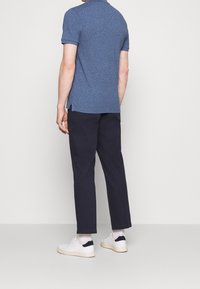 Blå pikétröja med korta ärmar, sidoflikar, i kombination med navybyxor och vita sneakers med mörka detaljer på hälen.