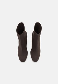 Stivali alla caviglia marroni con un design in tessuto aderente e slanciato. La punta affusolata e la costruzione senza cuciture mettono in evidenza una texture liscia.