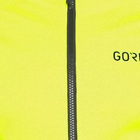 Helle gelbe Jacke mit einem zentralen schwarzen Reißverschluss und dem Text "GORE" in Schwarz. Glatte Textur aus einem strapazierfähigen, leichten Material.