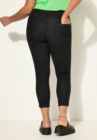 Zwarte denim capri jeans met een slim fit, twee achterzakken en een middelhoge taille. Gecombineerd met zwarte platform sandalen.
