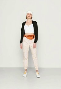 Cardigã preto, top curto branco, calças de carga bege e pochete laranja. Gorro de malha branco e ténis com detalhes amarelos.