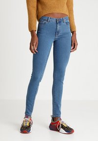 Smal blåjeans gjorda av denim med en slät yta, i en stil med medelhög midja och minimal sömnadsdetaljer, ihopparat med färgglada sneakers.