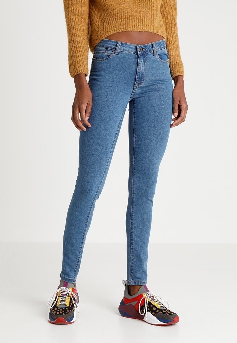 Smal blåjeans gjorda av denim med en slät yta, i en stil med medelhög midja och minimal sömnadsdetaljer, ihopparat med färgglada sneakers.