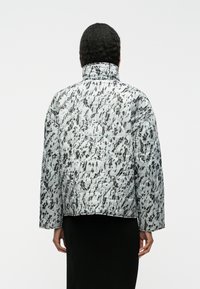 Επενδεδυμένο μπουφάν με αφηρημένο μοτίβο σε μαύρο και λευκό, με ψηλό γιακά, ραφές και χαλαρή εφαρμογή.