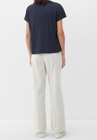 Tummansininen lyhythihainen paita rentoa leikettä ja teksturoitua kangasta, yhdistettynä luonnonvalkoisiin leveälahkeisiin housuihin ja vaaleisiin kenkiin.