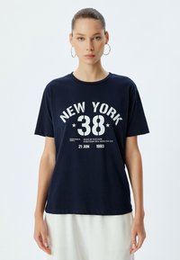 Camiseta de algodón azul marino con un estampado gráfico blanco que dice "NEW YORK 38" y texto adicional. Manga corta, escote redondo, corte holgado.