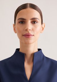 Navy blue top with a high collar, featuring a smooth texture and clean design. Close-up view focusing on the neckline and fabric details.