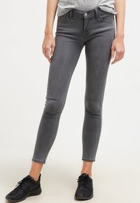 Jeans skinny de denim gris con una cintura de talle medio, diseño de cinco bolsillos y un desgaste sutil. Combinados con zapatillas deportivas negras.